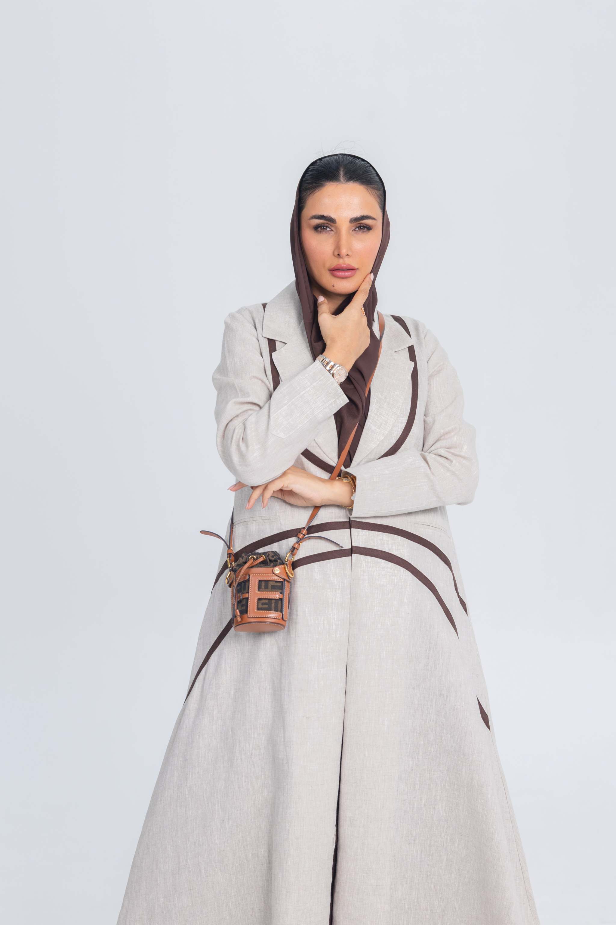 Woman wearing SandShell beige linen abaya with brown brim detailing and matching brown headscarf against white background