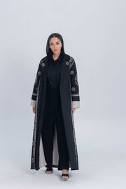 Woman wearing black luxury linen abaya with beige circular embroidery, standing against plain background