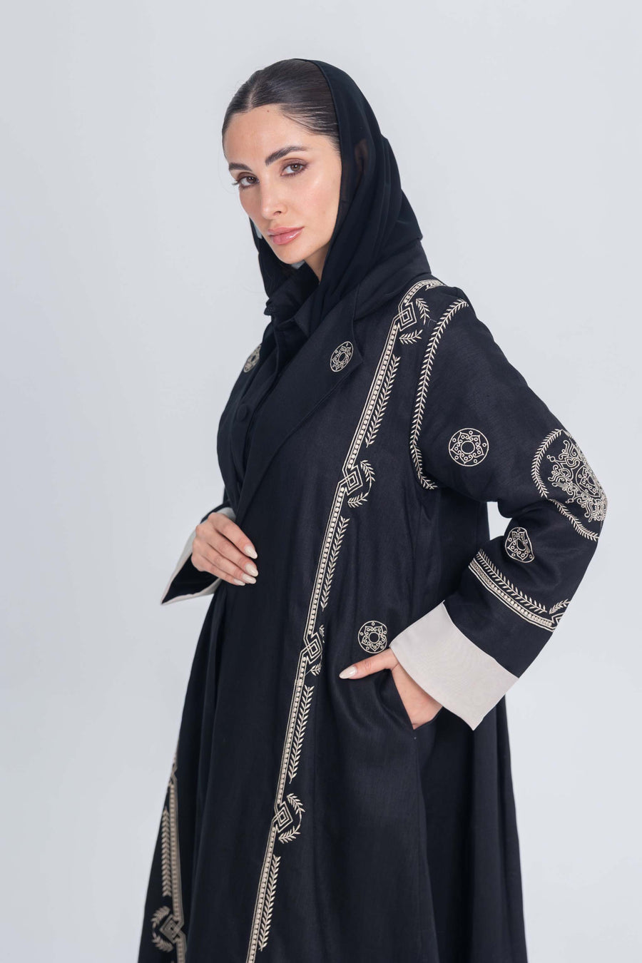 Black luxury linen abaya with intricate beige circular embroidery and machine-stitched detailing, worn by a woman in a black hijab.