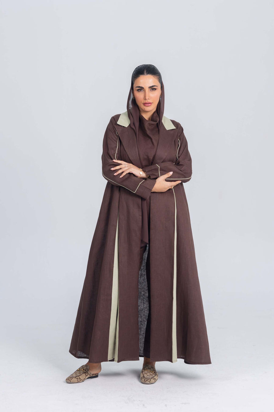 Woman wearing a brown linen abaya with soft mint green panels and refined detailing standing against a plain background.