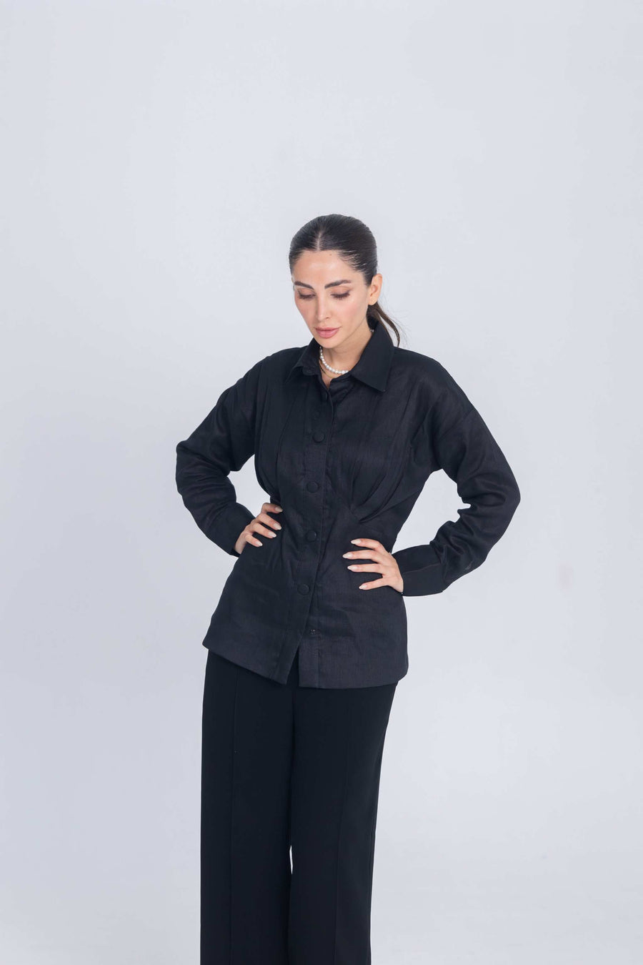 Woman wearing black Essence Folds shirt with chest pleats and black pants against plain background