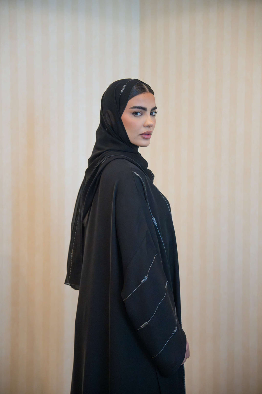 Woman wearing black relaxed fit Abaya with subtle gray arrow embroidery on sleeves and front, paired with matching black sheila headscarf-Abaya Features