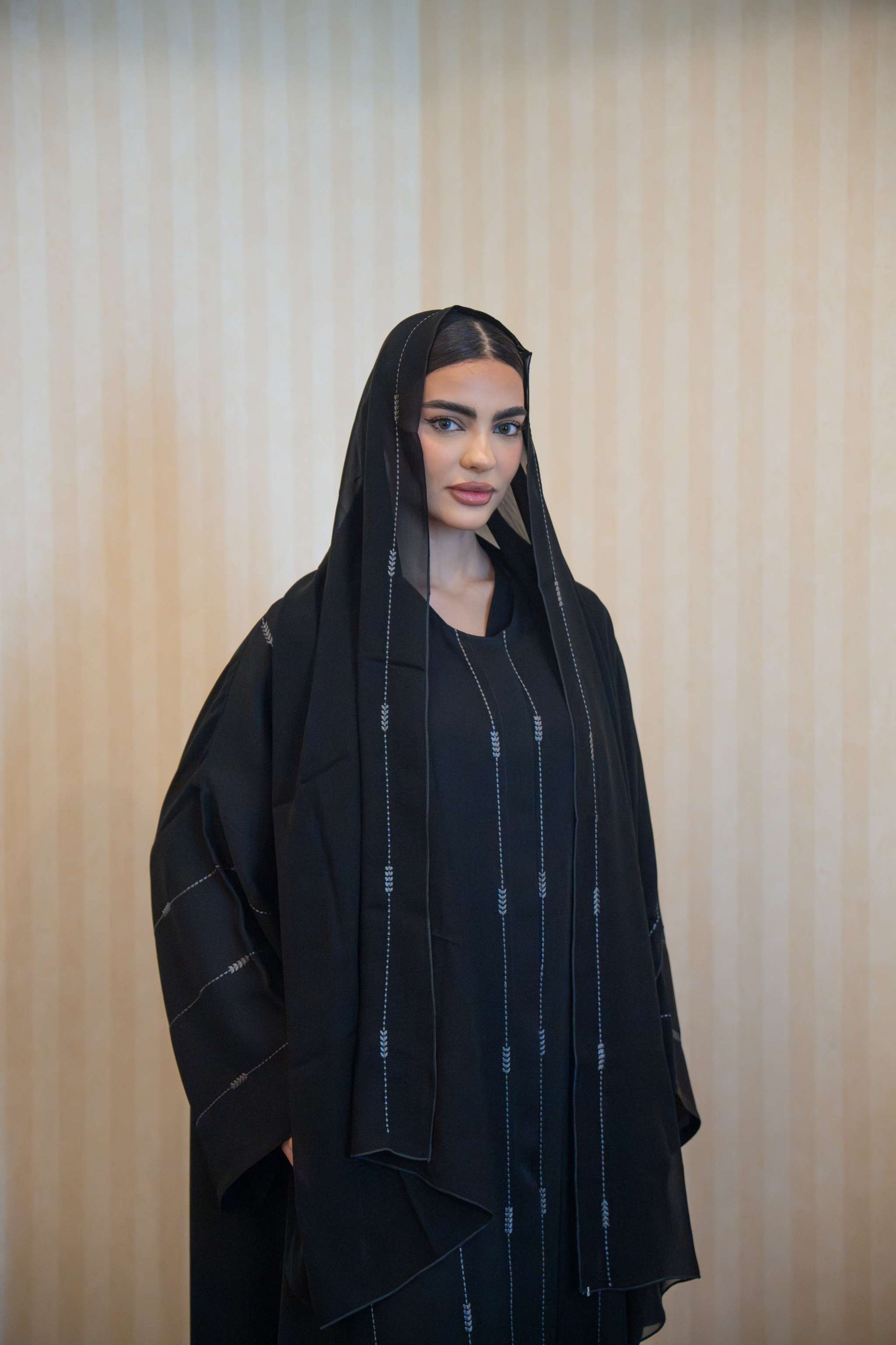 Woman wearing a black abaya with subtle gray embroidery and a matching embroidered sheila, featuring a relaxed fit and front buttons.