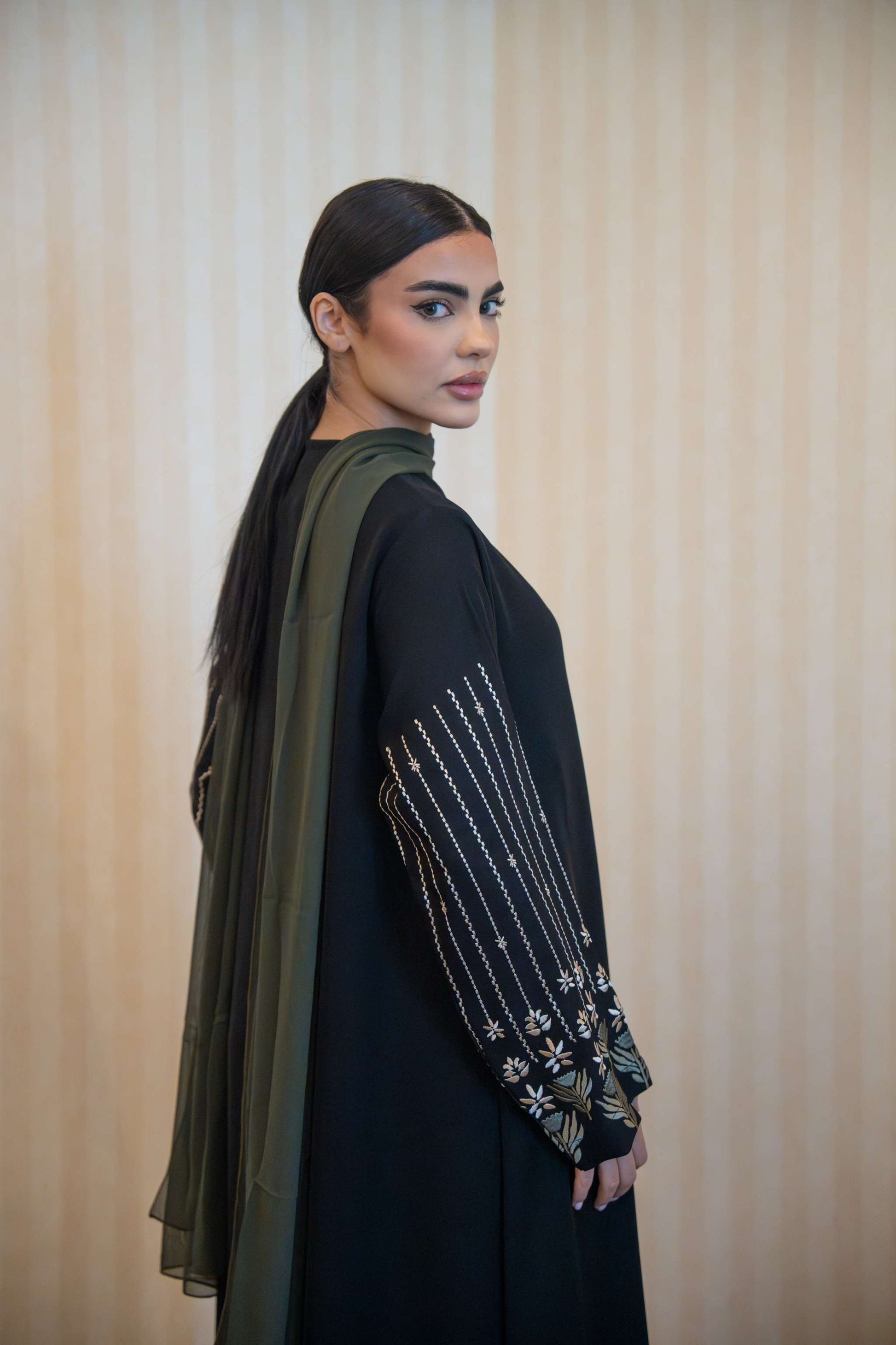 Black straight-cut abaya with floral embroidered sleeves and olive green trim, featuring a round neckline and front buttons.