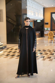 Black abaya with straight cut, round neckline, brown trim, and embroidered wide sleeves.