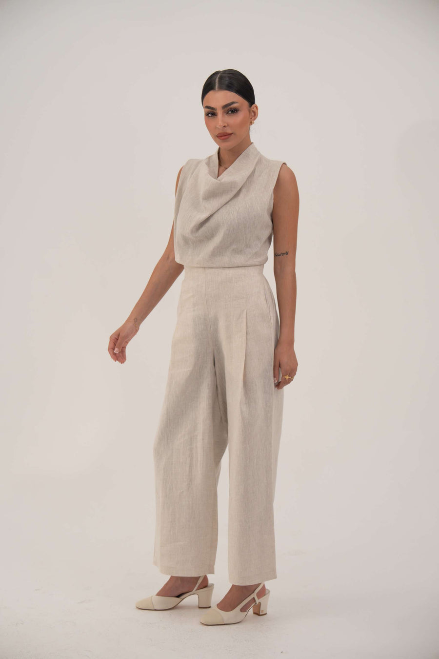 Woman wearing linen beige wide leg pants with a sleeveless top and heels against a plain background