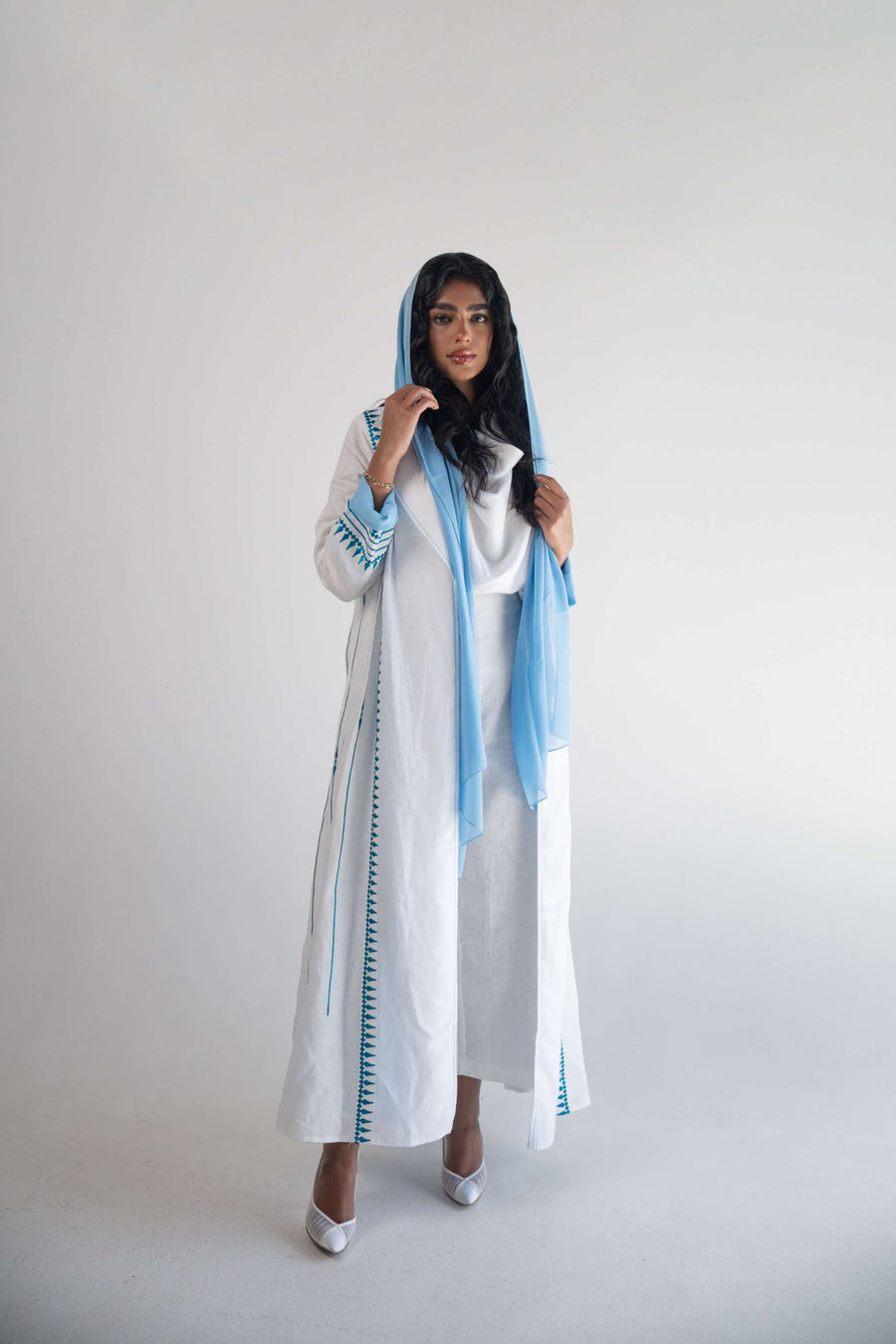 White linen blazer abaya with blue triangular embroidery and soft blue chiffon inner layer, worn with matching blue headscarf.