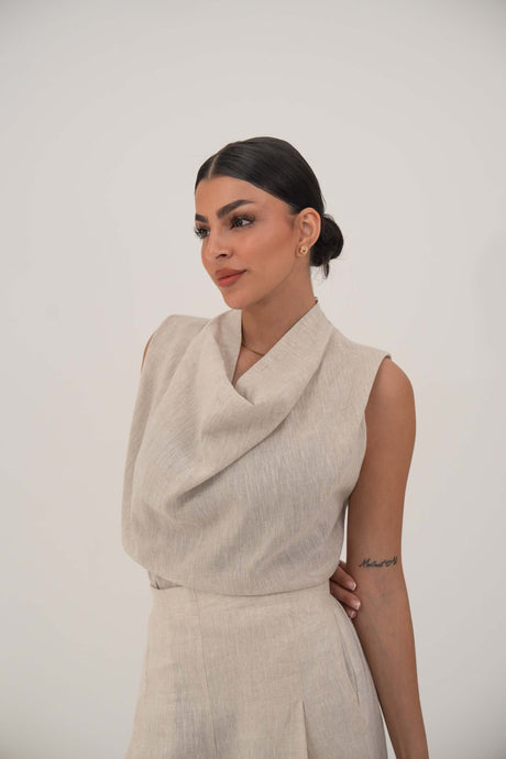Woman wearing a sleeveless beige blouse with a draped cowl neckline and high-waisted wide-leg pants