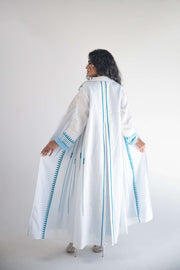 White linen blazer abaya with light blue triangular embroidery and chiffon inner layer, featuring pleats for graceful movement.