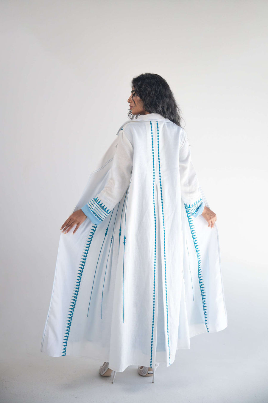 White linen blazer abaya with light blue triangular embroidery and chiffon inner layer, featuring pleats for graceful movement.