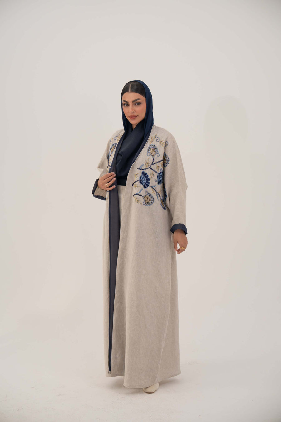woman wearing a premium linen abaya with navy floral embroidery and gold accents in a soft beige color