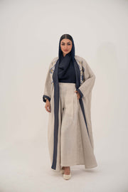 woman wearing a premium linen abaya with navy floral embroidery and gold accents in a soft beige color