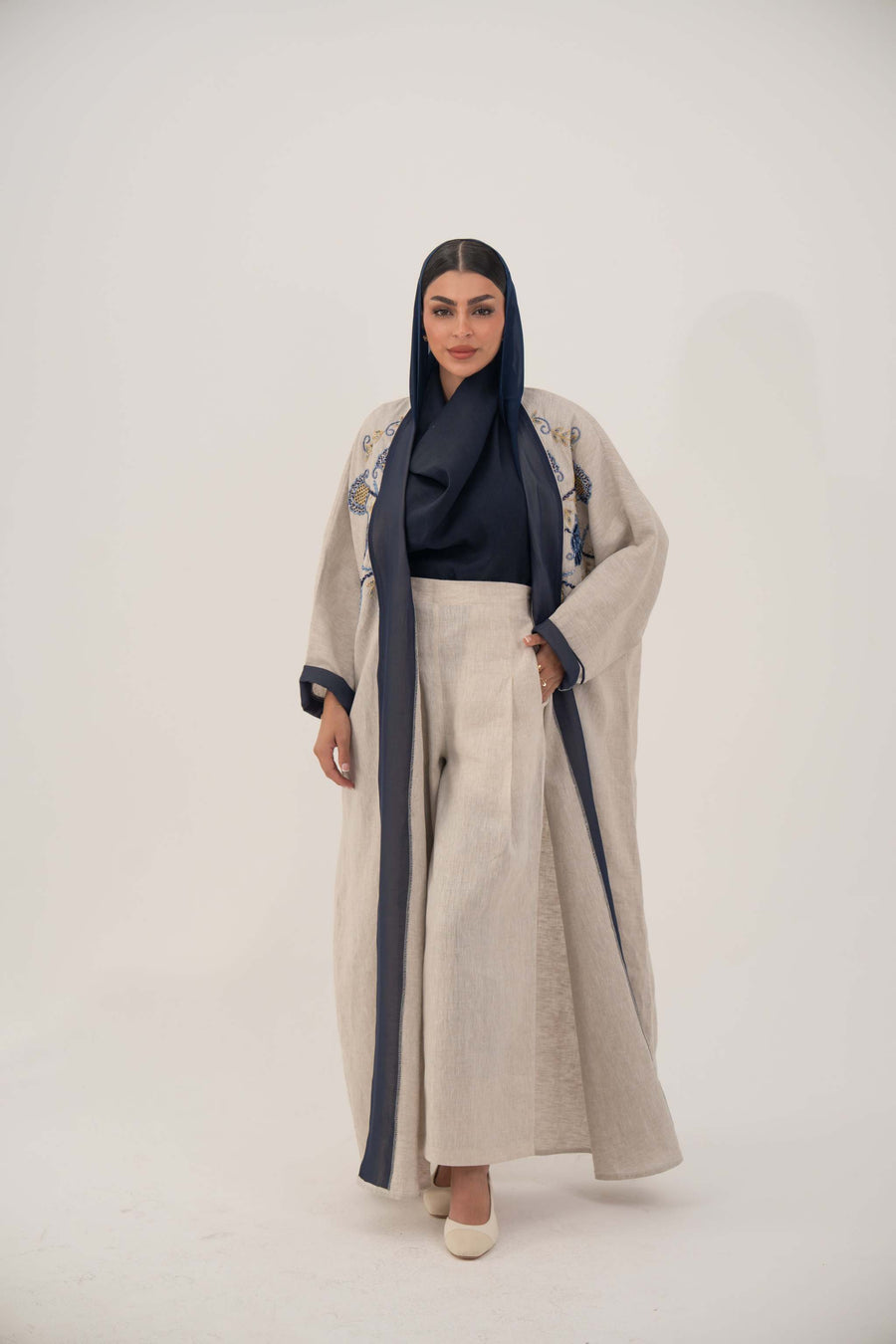 woman wearing a premium linen abaya with navy floral embroidery and gold accents in a soft beige color