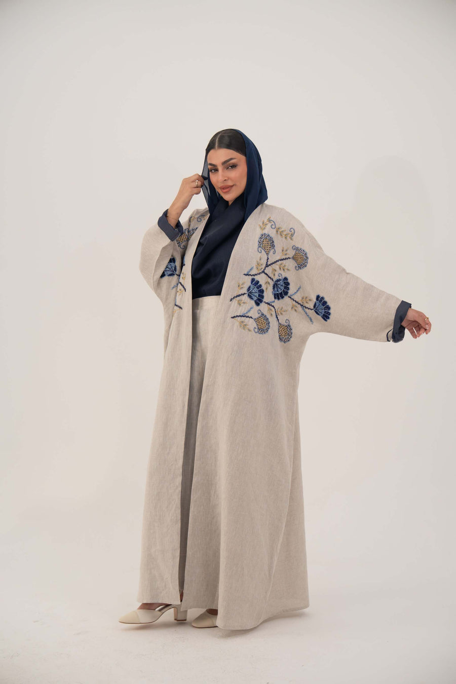 woman wearing a premium linen abaya with navy floral embroidery and gold accents in a soft beige color