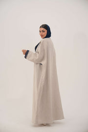 woman wearing a premium linen abaya with navy floral embroidery and gold accents in a soft beige color