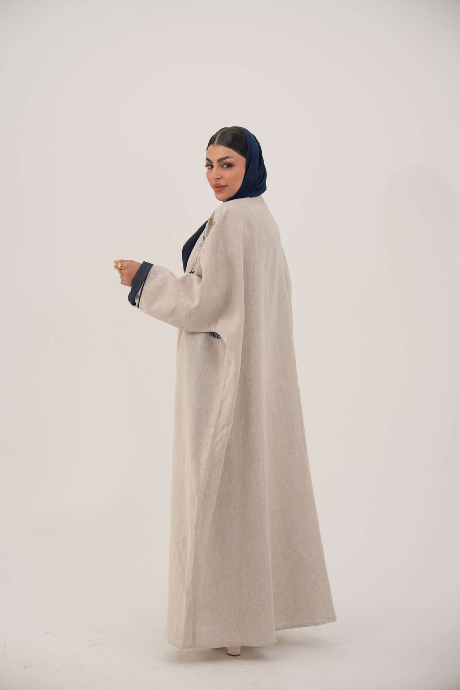 woman wearing a premium linen abaya with navy floral embroidery and gold accents in a soft beige color