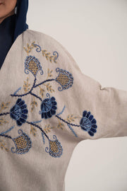 woman wearing a premium linen abaya with navy floral embroidery and gold accents in a soft beige color