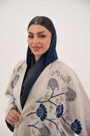 woman wearing a premium linen abaya with navy floral embroidery and gold accents in a soft beige color