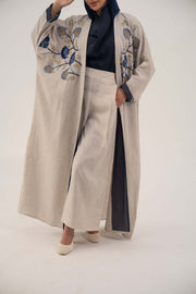 woman wearing a premium linen abaya with navy floral embroidery and gold accents in a soft beige color