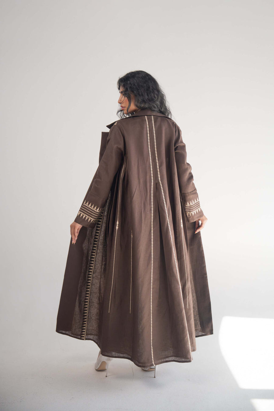 Woman wearing a dark brown linen blazer abaya with beige triangular embroidery and blazer collar, styled with a light beige chiffon inner layer and subtle back pleats.