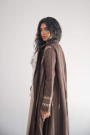 Woman wearing a dark brown linen blazer abaya with beige triangular embroidery and blazer collar, styled with a light beige chiffon inner layer and subtle back pleats.
