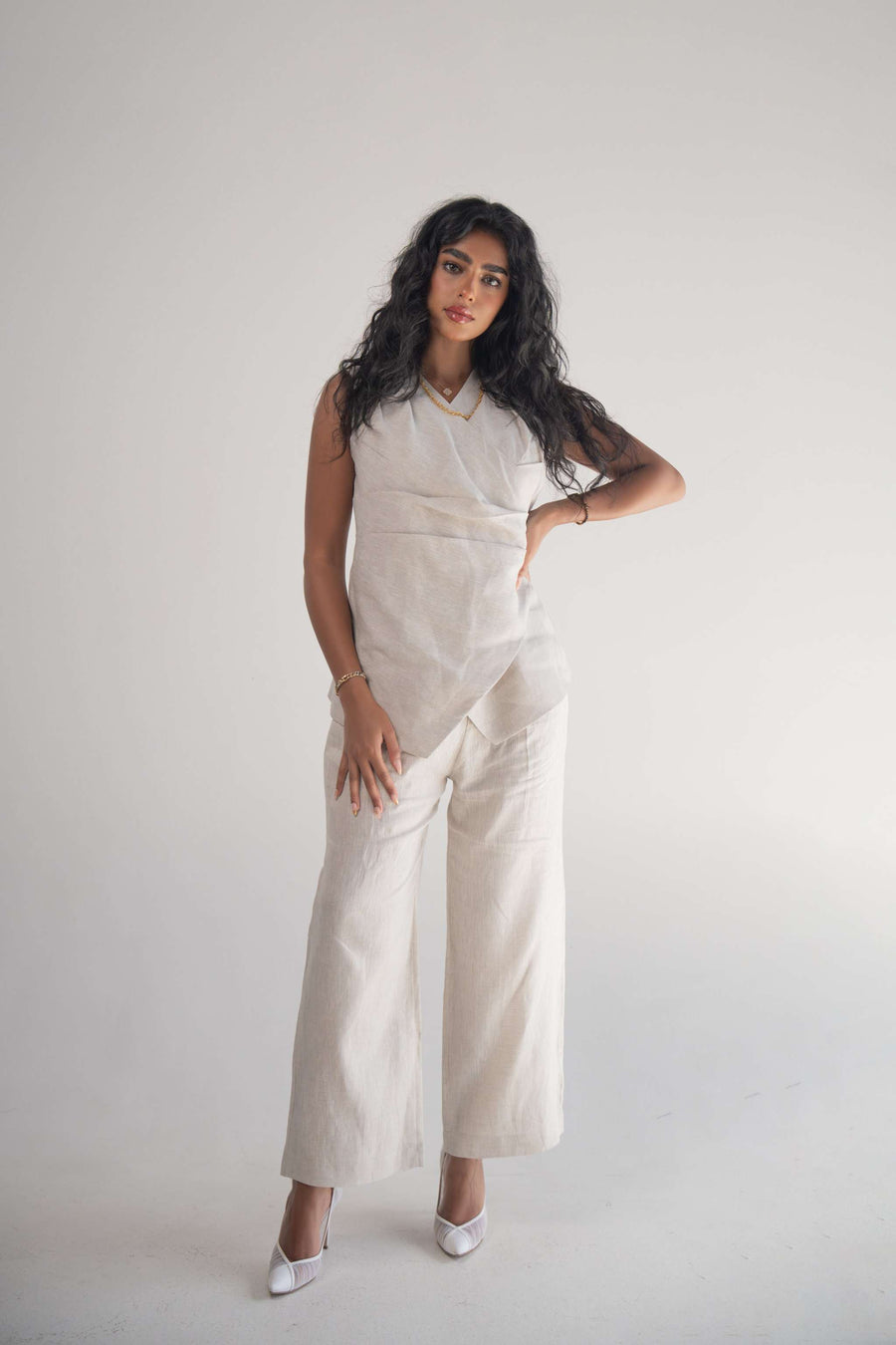 Woman wearing sleeveless almond beige blouse with wrapped front and soft pleats paired with matching wide-leg pants