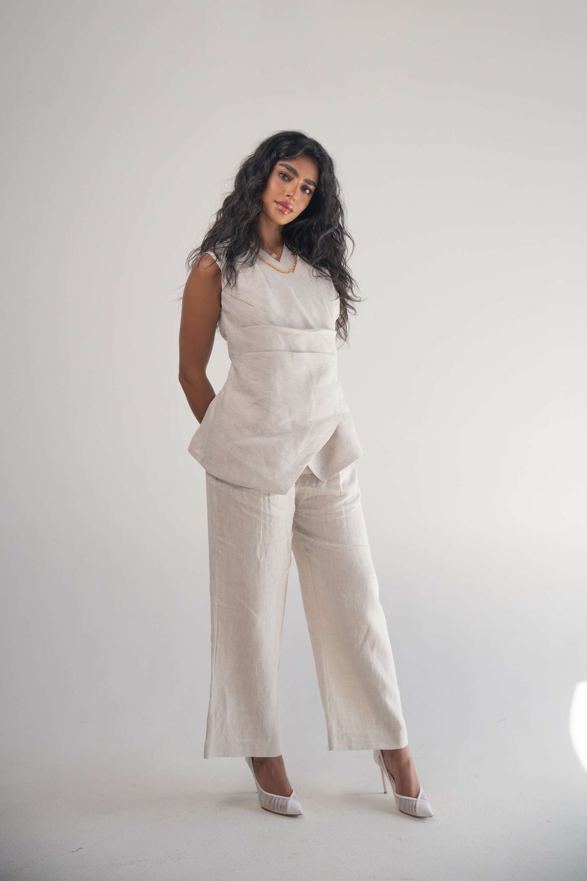 Woman wearing sleeveless Almond Beige Blouse with front wrap and pleated hem, paired with matching wide-leg pants.