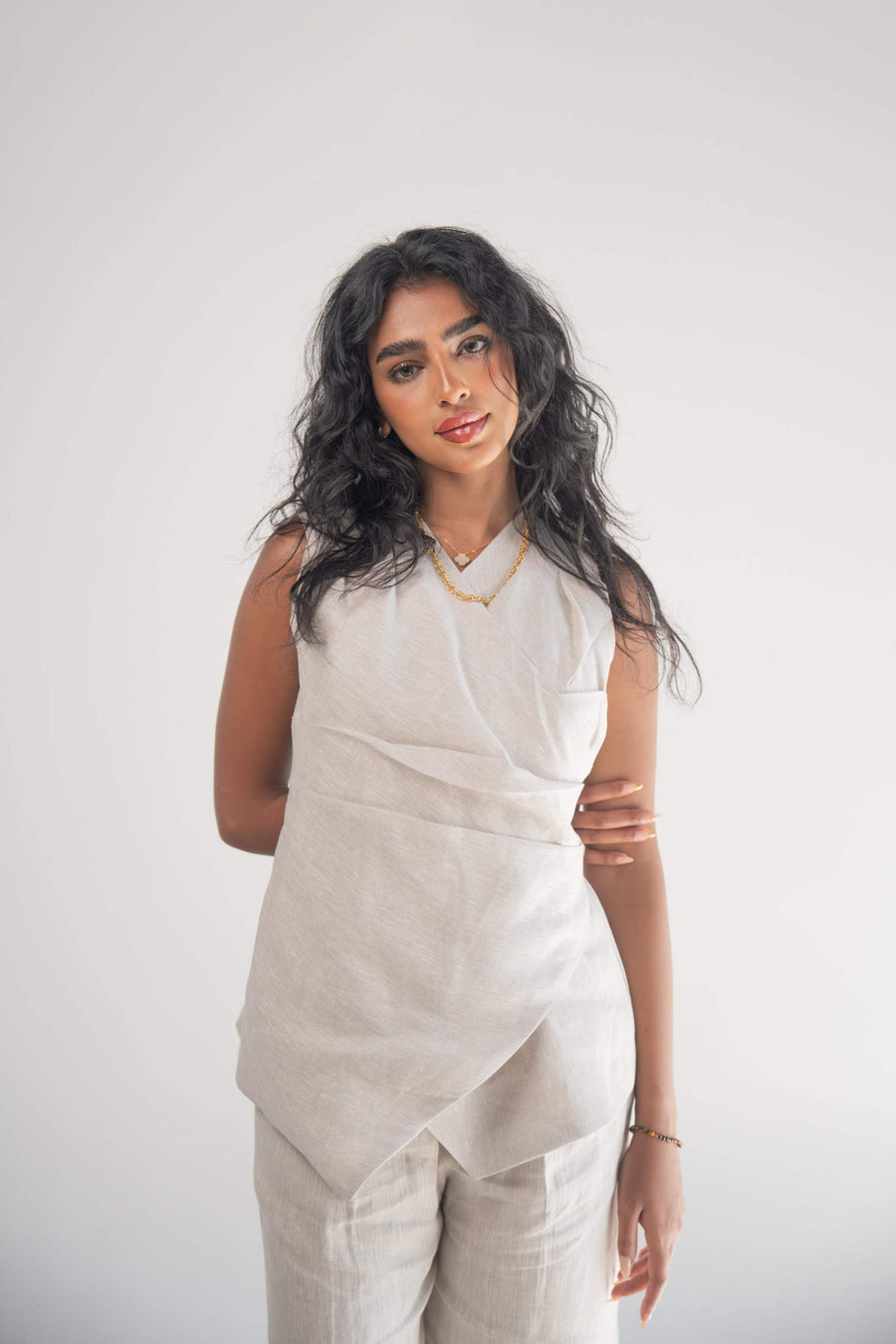 Woman wearing sleeveless Almond Beige Blouse with wrapped front and subtle pleated hem detail.