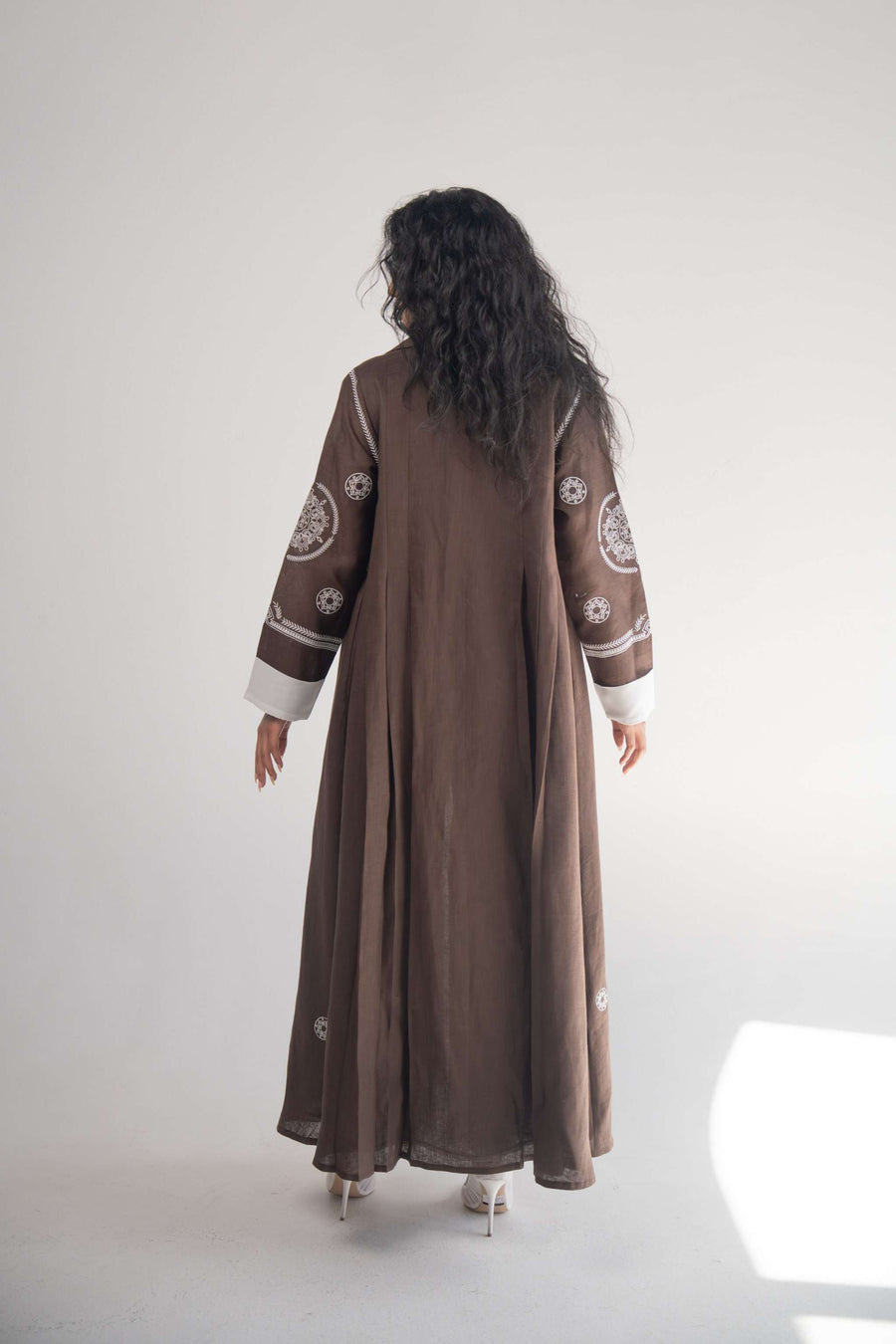 Back view of a cocoa linen blazer abaya with white circular and geometric embroidery on sleeves, sides, and back, featuring subtle pleats and white chiffon lining.