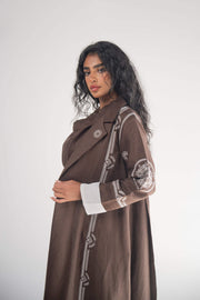 Woman wearing a cocoa brown linen blazer abaya with white geometric and circular embroidery on sleeves and sides, featuring a classic blazer lapel and white chiffon lining.