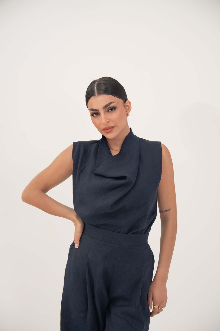 Woman wearing sleeveless navy blue blouse with draped cowl neckline and matching high-waisted pants