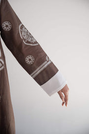 Close-up of a rich brown linen blazer abaya sleeve with elegant white circular and geometric embroidery and soft white chiffon lining.