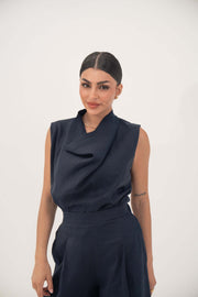 Woman wearing a sleeveless navy blue linen blend blouse with a draped cowl neckline and high-waisted pants