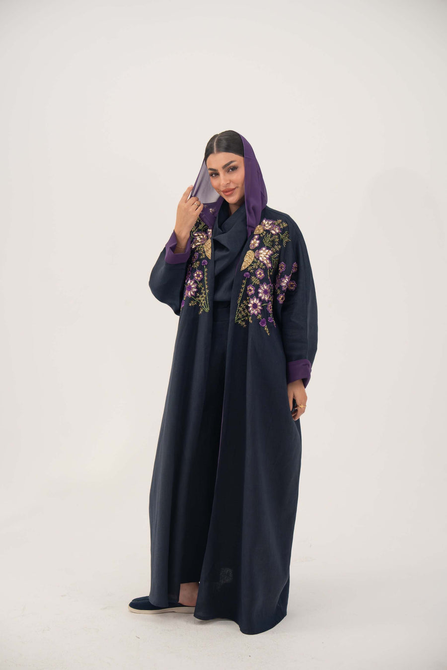woman wearing navy blue linen-blend abaya with purple, gold, and green hand-stitched floral details and purple cuffs