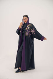 Navy blue linen-blend abaya with purple, gold, and green hand-stitched floral details and wide bisht style with purple cuffs and chiffon lining.