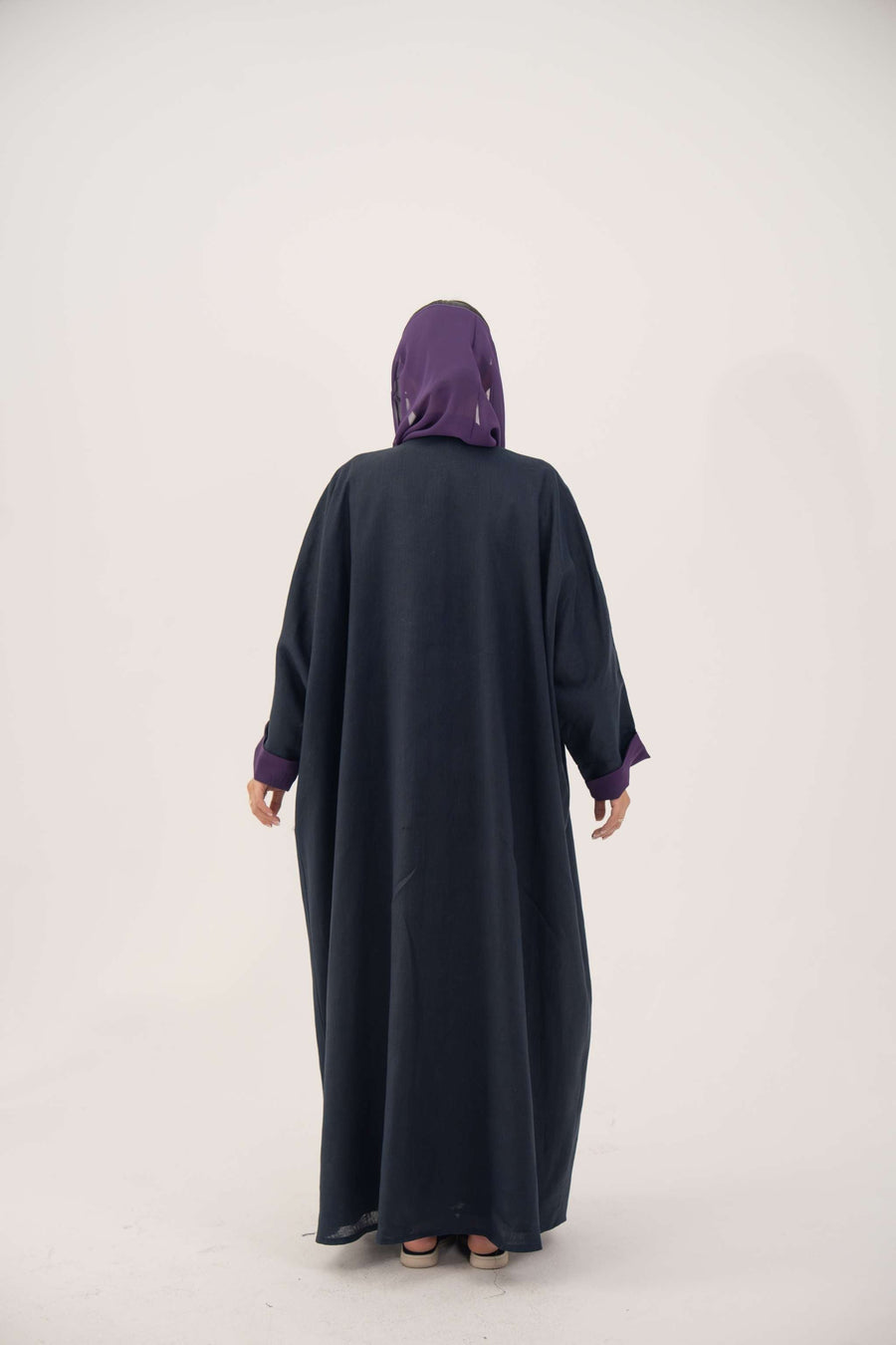 Back view of a navy blue linen-blend abaya with purple cuffs and a matching inner border, featuring a loose bisht style and lightweight lining.