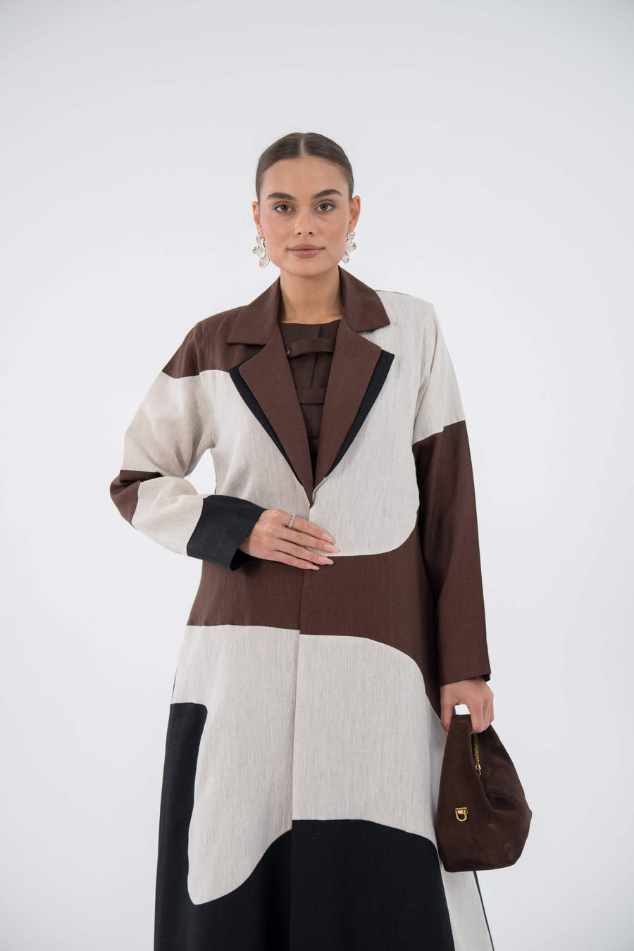 Woman wearing Desert Waves Blazer Abaya made of lightweight linen with beige, brown, and black wave panels holding a brown bag