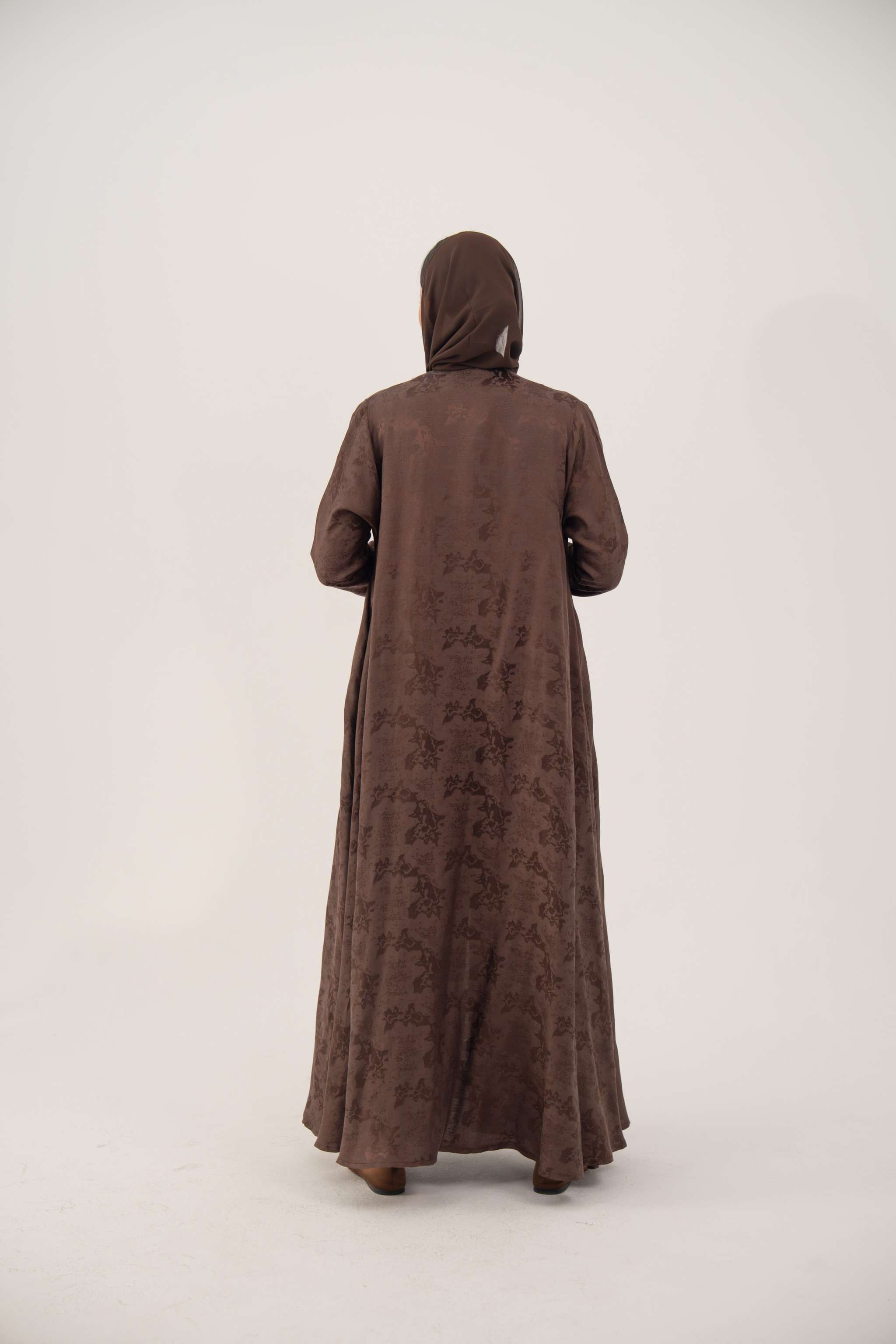 Back view of a full-length A-line jacquard silk abaya in warm cocoa brown with subtle woven floral pattern and long sleeves