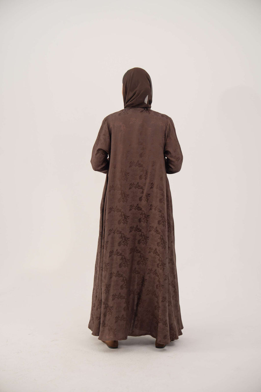 Back view of a full-length A-line jacquard silk abaya in warm cocoa brown with subtle woven floral pattern and long sleeves