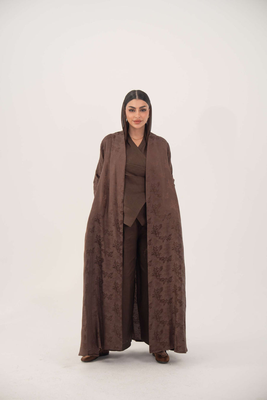 Woman wearing a full-length jacquard silk abaya with subtle floral pattern in warm cocoa brown color.