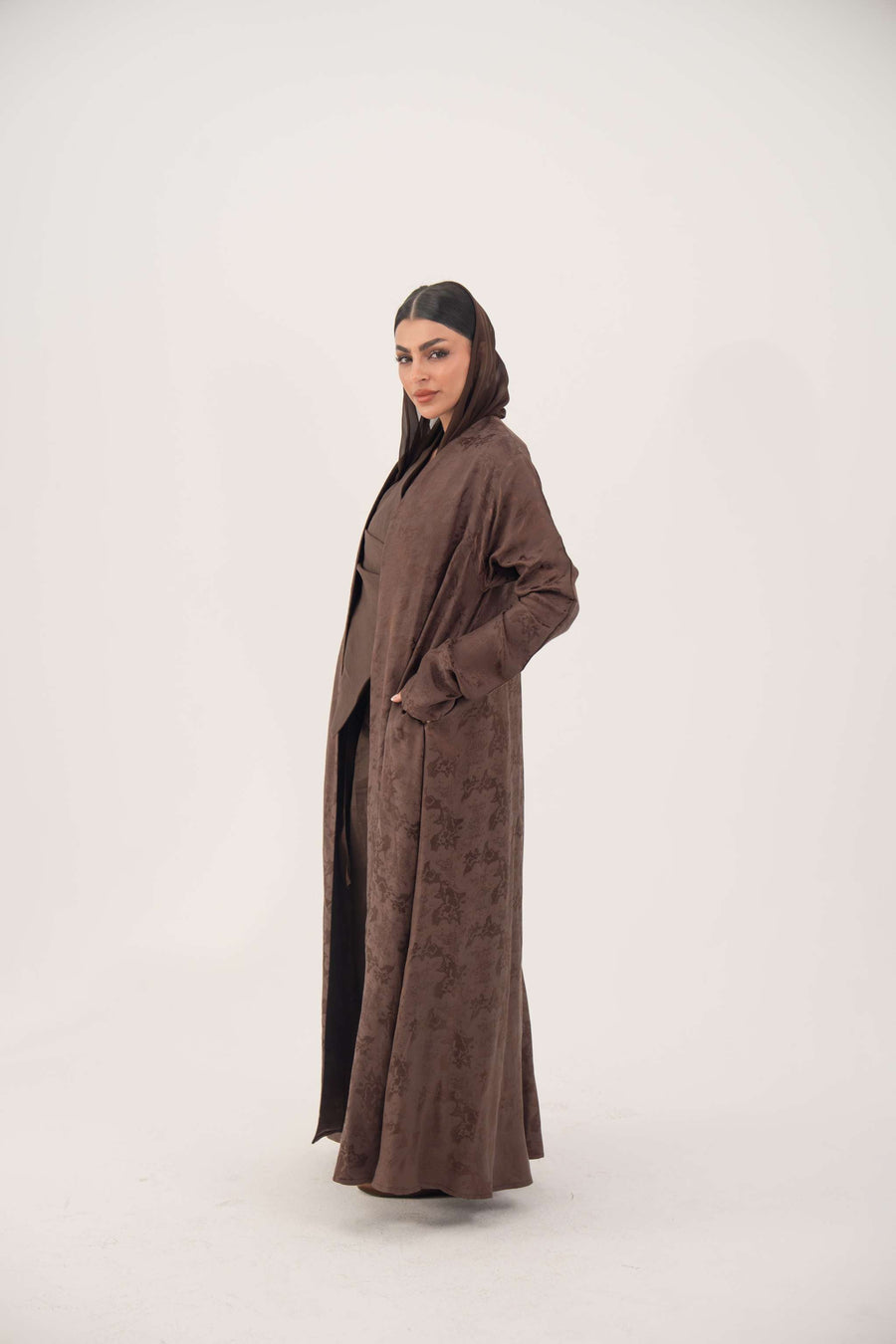Full-length jacquard silk abaya in warm cocoa brown with subtle woven floral pattern and long sleeves.