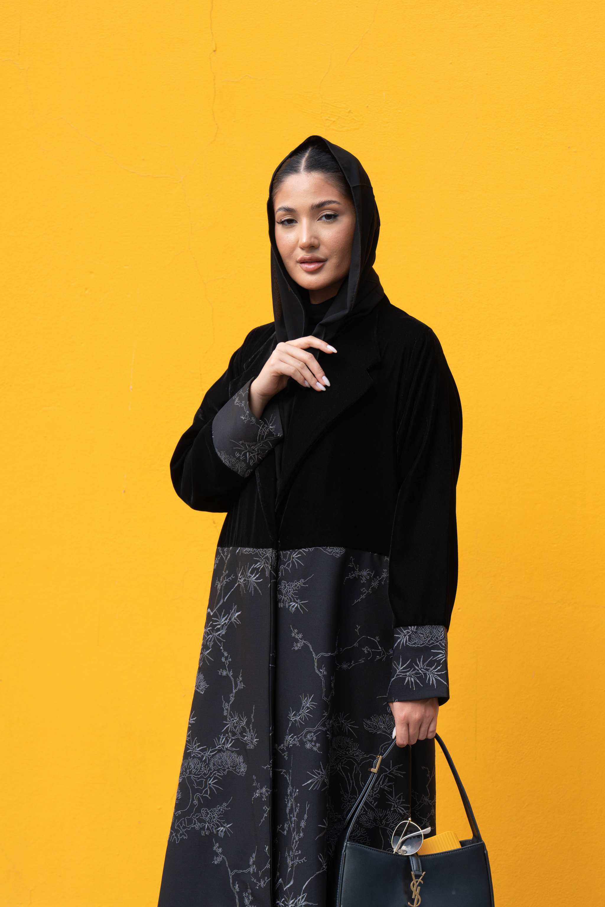 luxurious black abaya made of velvet with crepe embroidery, worn by woman against yellow background