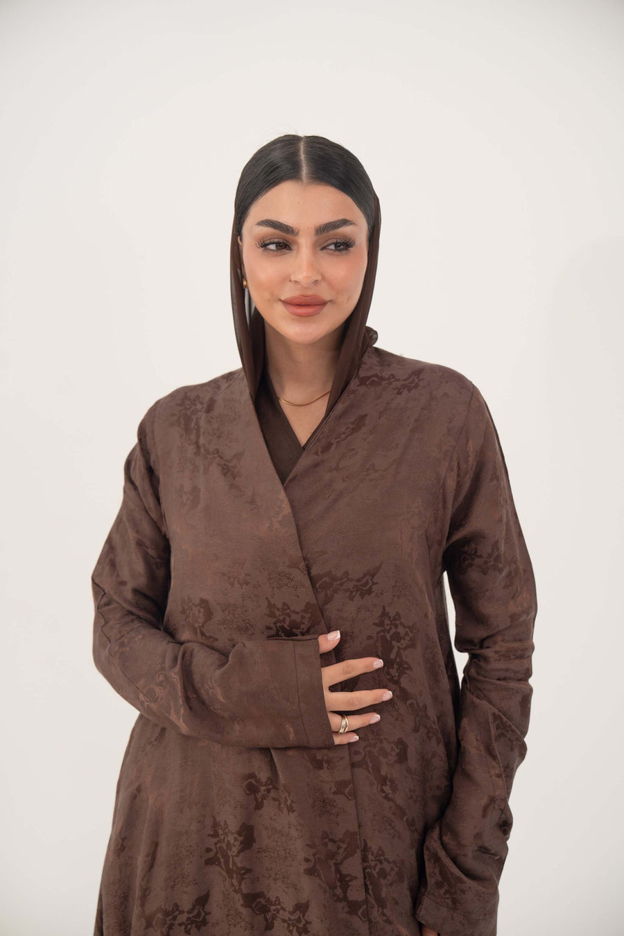 woman wearing a full-length relaxed A-line jacquard silk abaya with subtle floral pattern and long sleeves in warm cocoa brown
