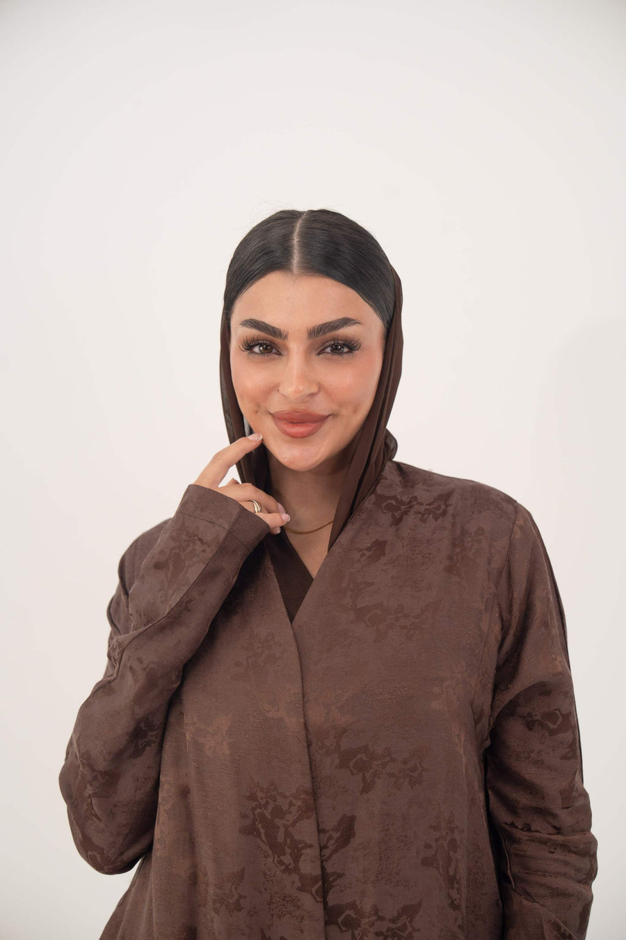 Woman wearing a warm cocoa brown jacquard silk abaya with subtle floral pattern and long sleeves in a relaxed A-line cut.