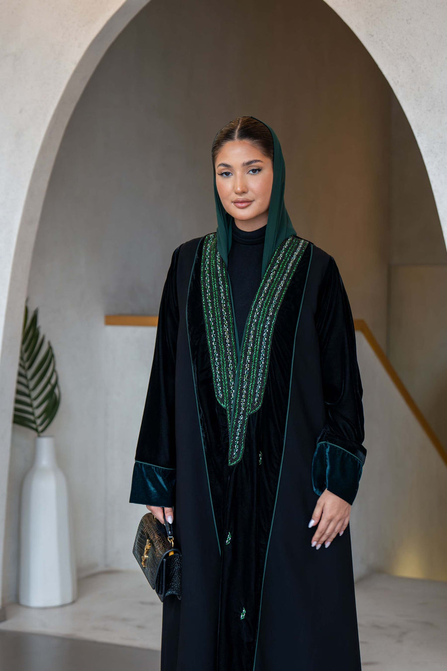woman wearing statement black abaya with green hand embroidery velvet cuffs and matching green scarf in elegant setting