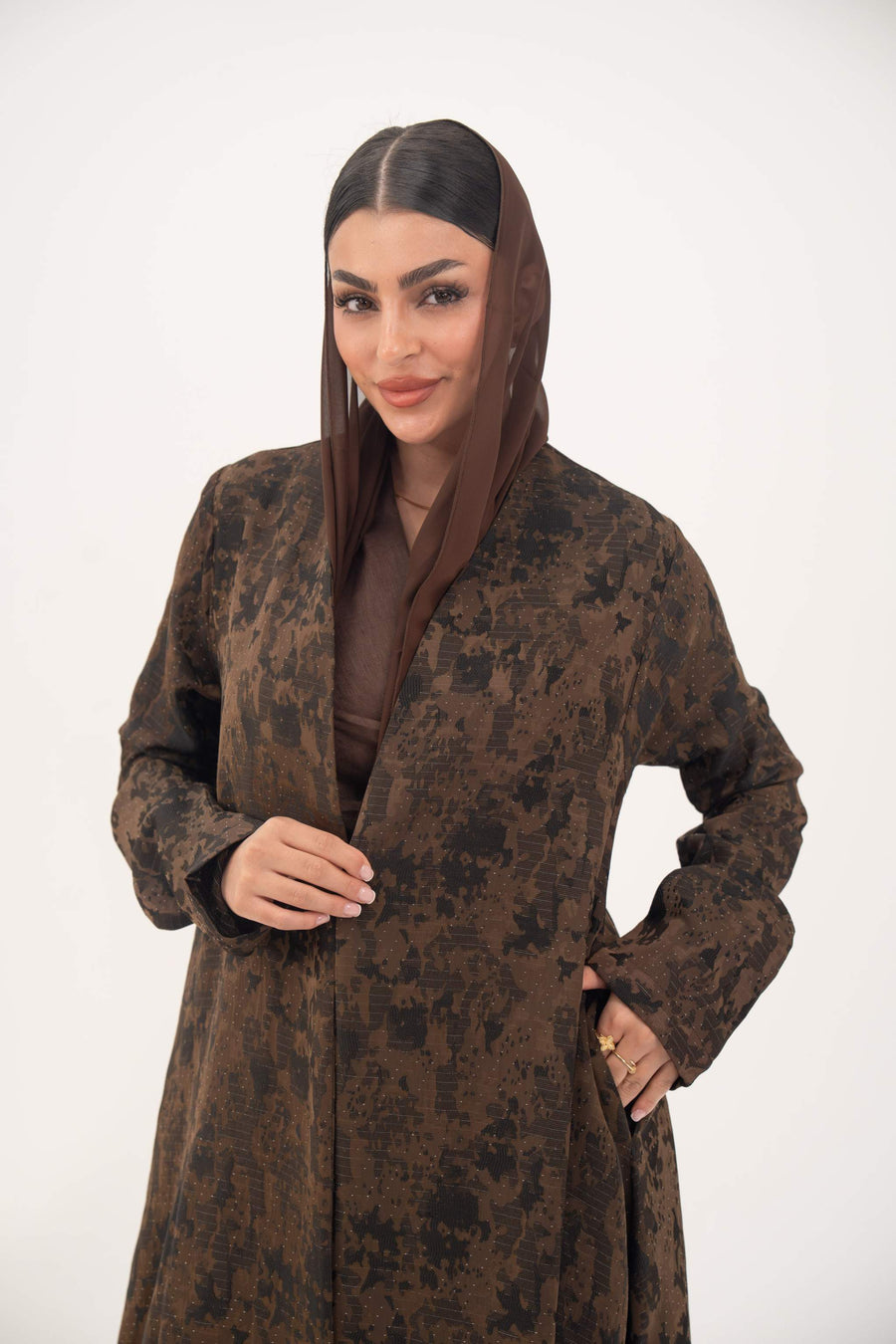 Woman wearing a lightweight espresso brown jacquard silk abaya with subtle tonal pattern, open front, side pockets, and full-length sleeves.