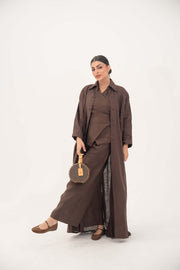 Woman wearing deep cocoa brown linen shirt-inspired abaya with classic collar and tonal buttons, holding round handbag.
