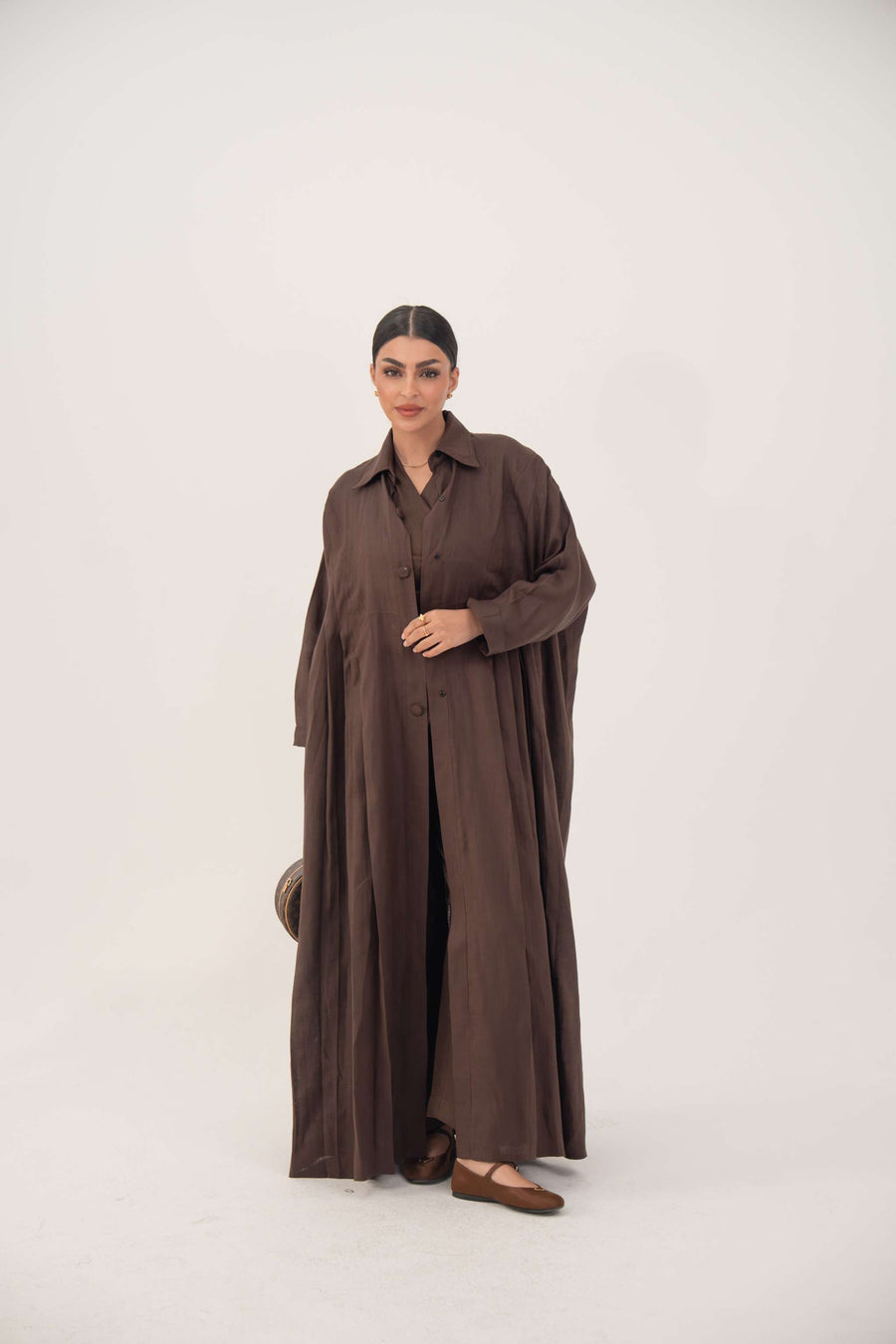 Woman wearing deep cocoa brown linen shirt-inspired abaya with button-down front and relaxed long sleeves.