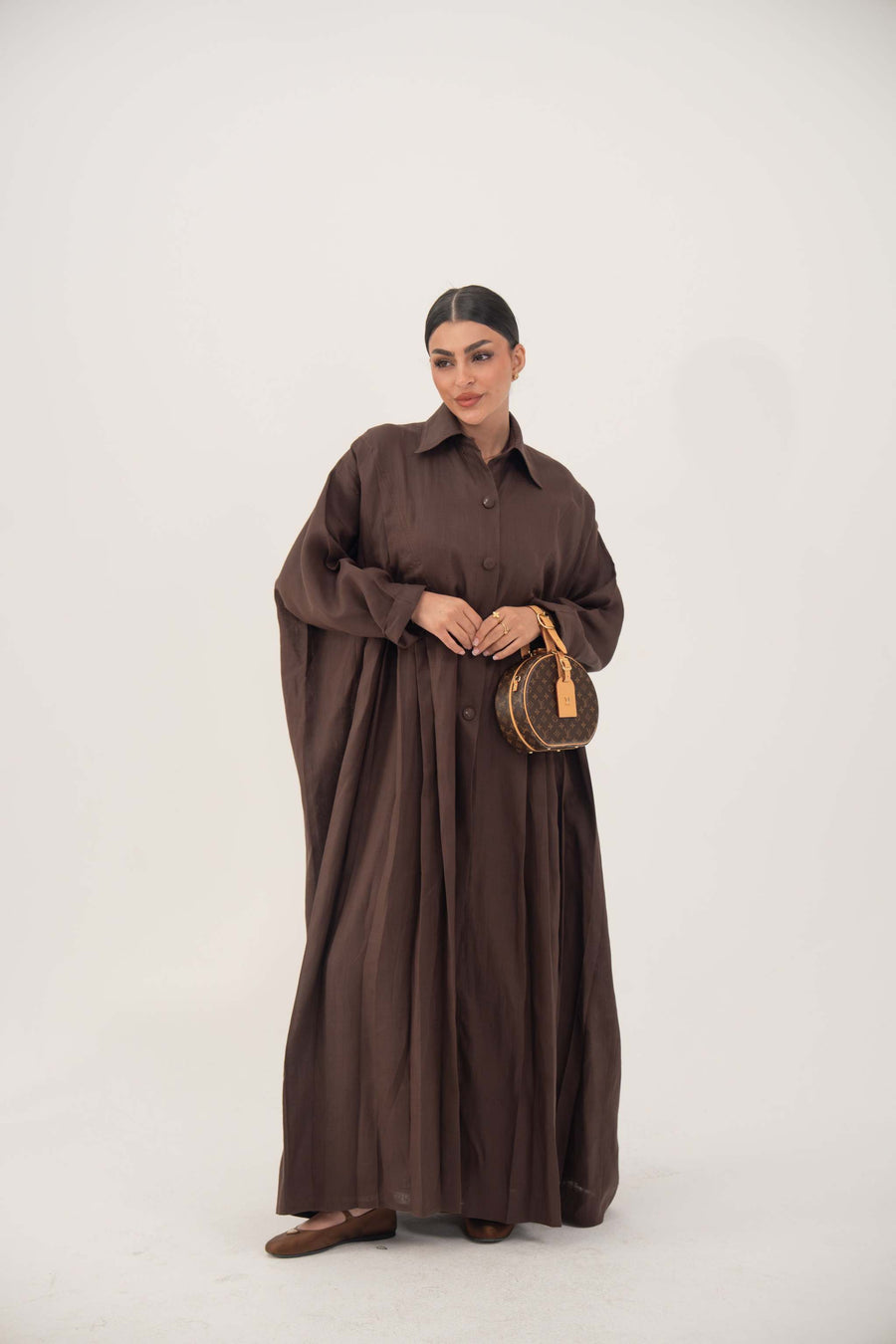 Woman wearing deep cocoa brown linen shirt-inspired abaya with classic collar and button-down front holding a small round handbag