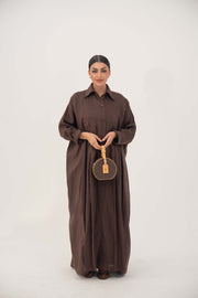 Woman wearing a deep cocoa brown linen shirt-style abaya with long sleeves and button-down front, holding a round brown handbag.